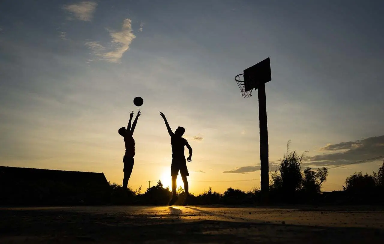 To personer spiller basketball i solnedgang